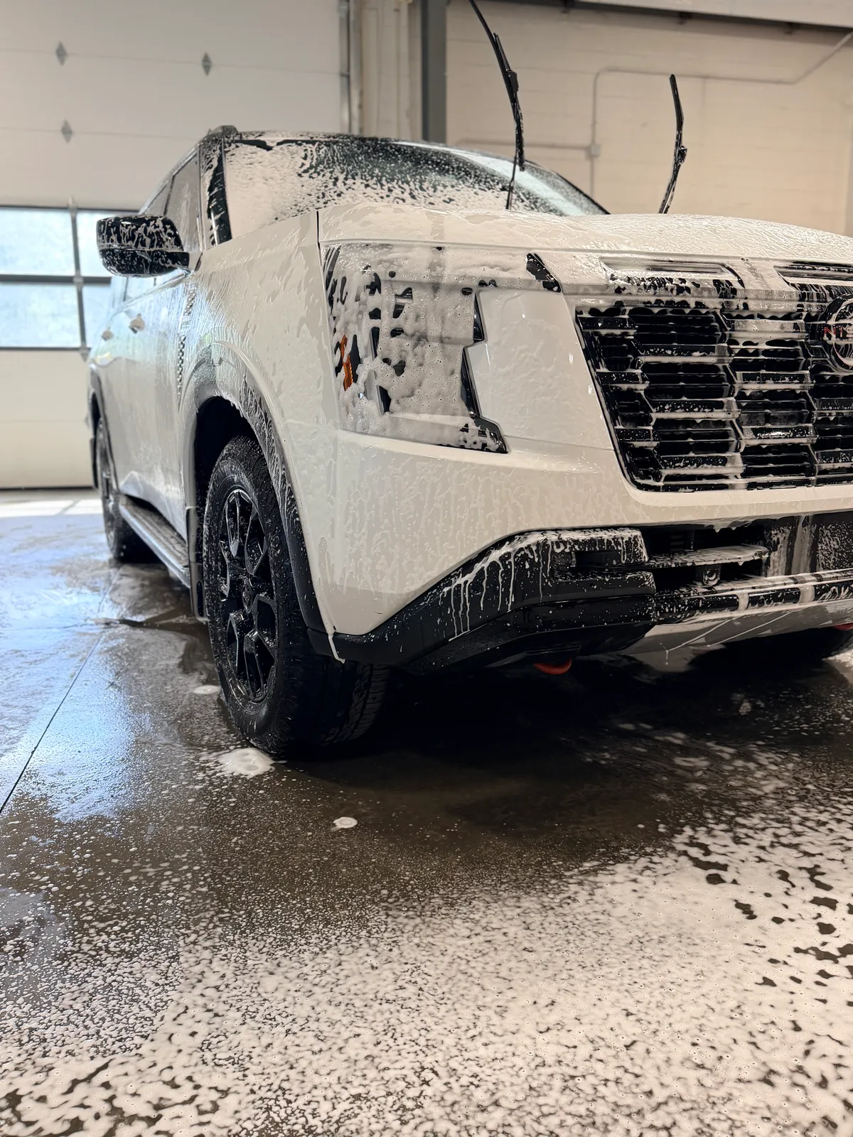 The front of a white SUV covered in foam during a hand wash.