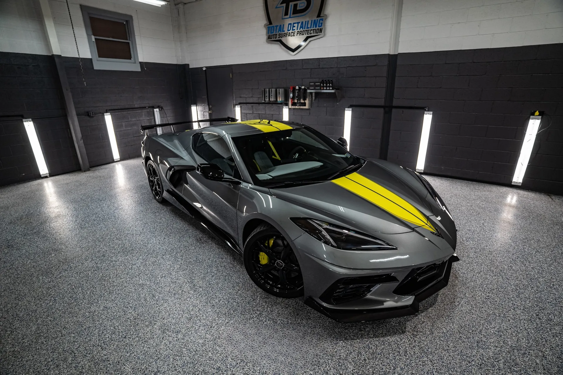 A gray Corvette with a yellow stripe under the inspection lights in our bay after a detail.