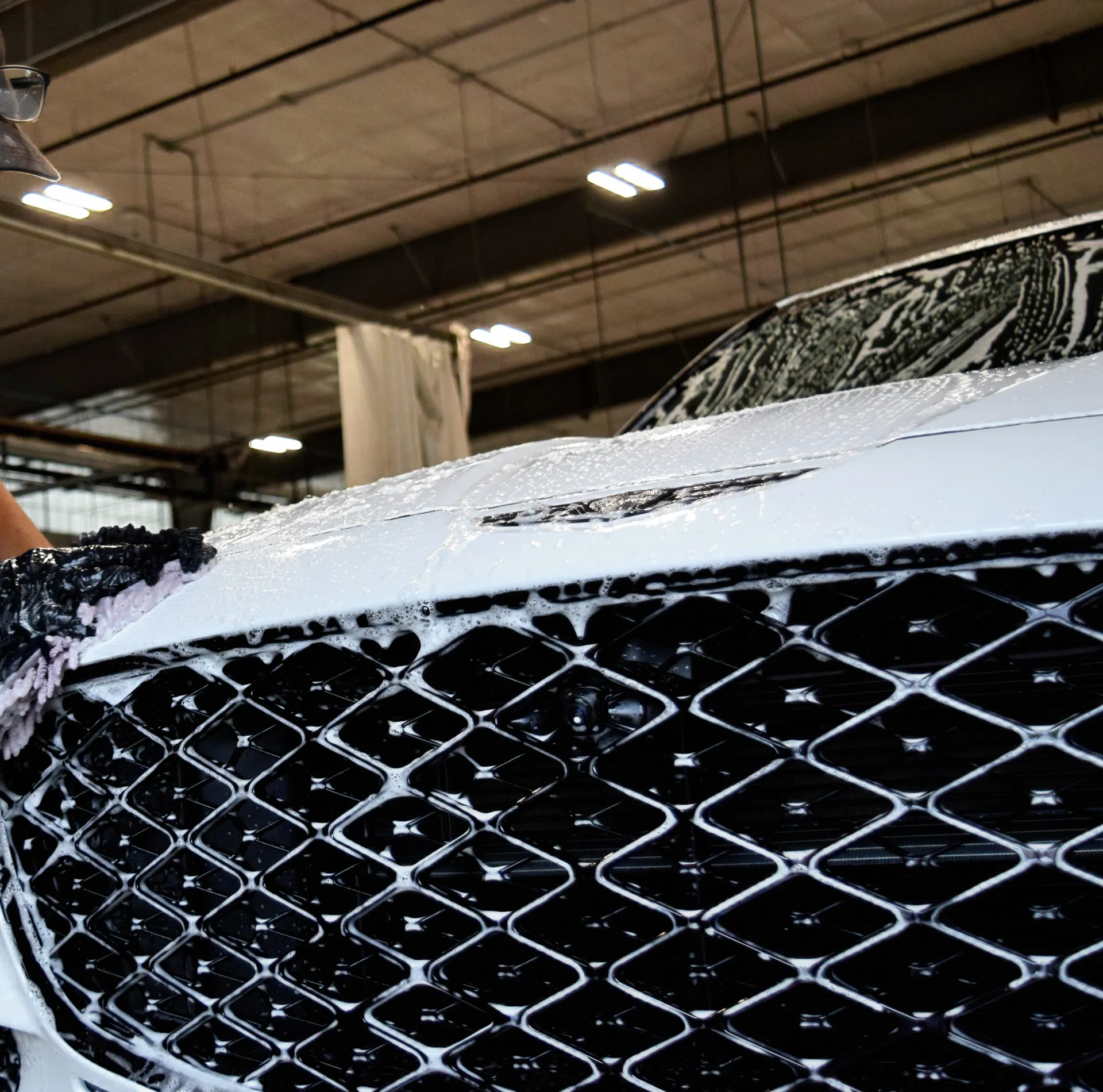 Gloved hands working foam into a chrome grille by hand.