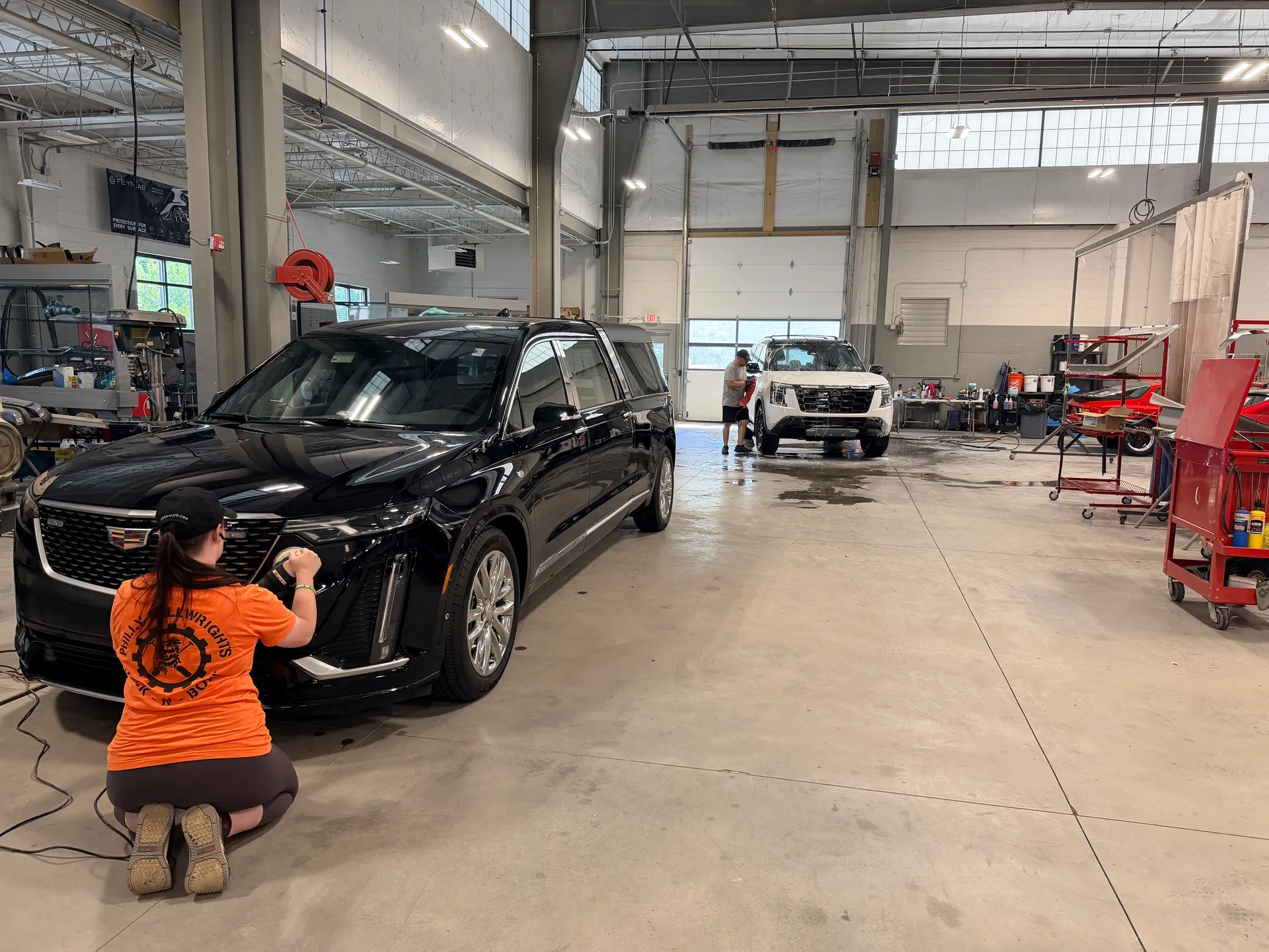 A technician working the front of a black SUV in the detail bay.
