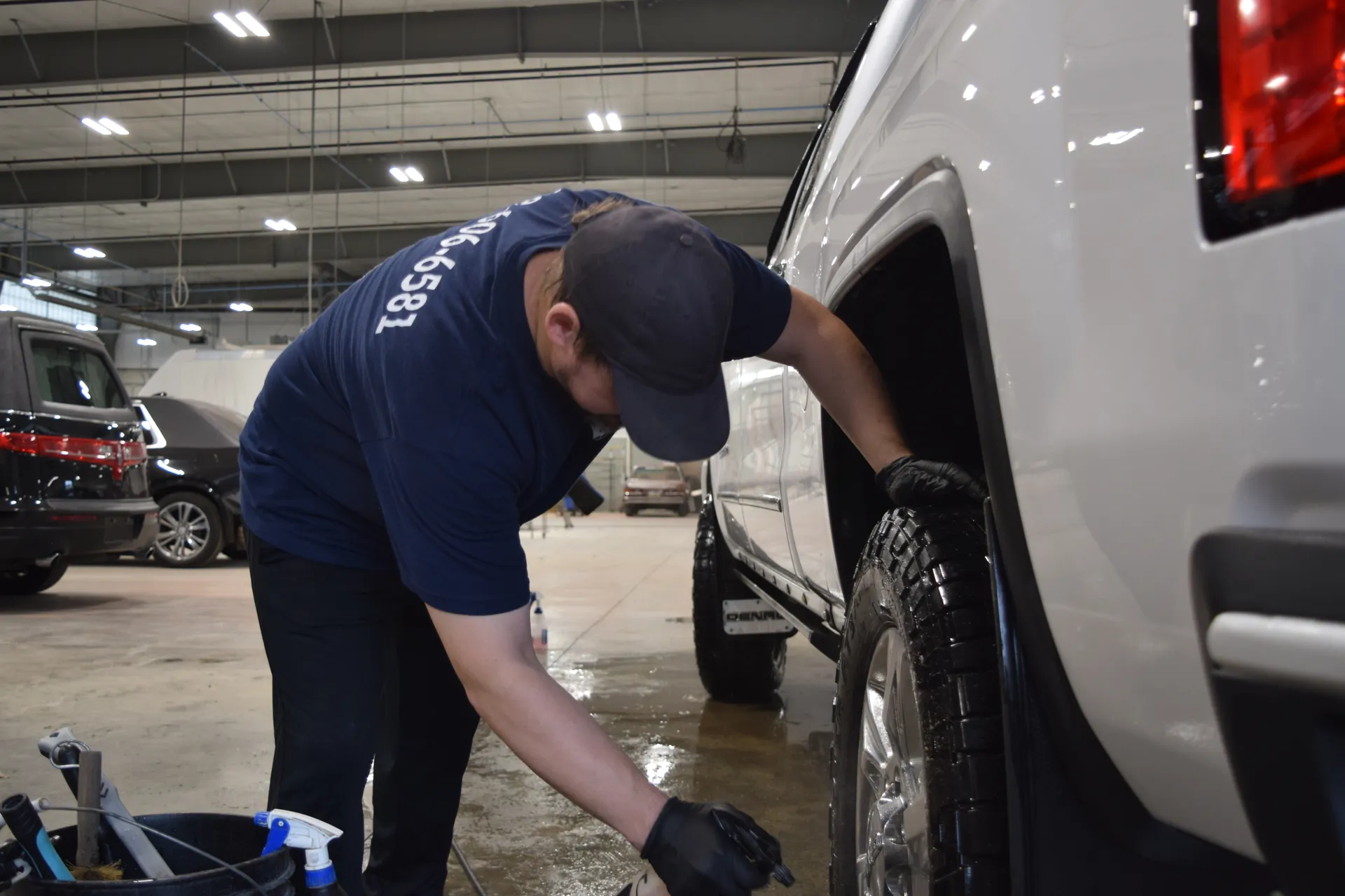 A technician dressing the tire and cleaning the wheel well on a white pickup.