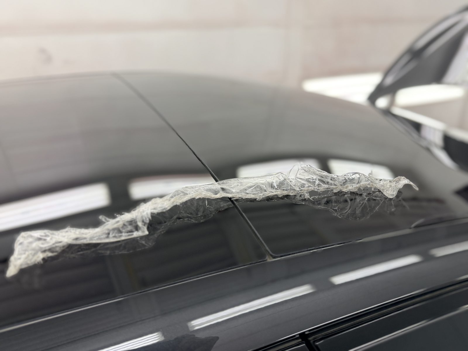 Aged paint protection film peeled up and bunched along the roof edge of a grey Lucid Air during removal in our shop.