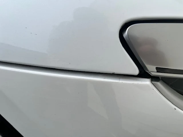 Close view of a sheet film edge running along a door crease, with road grime collected in the line