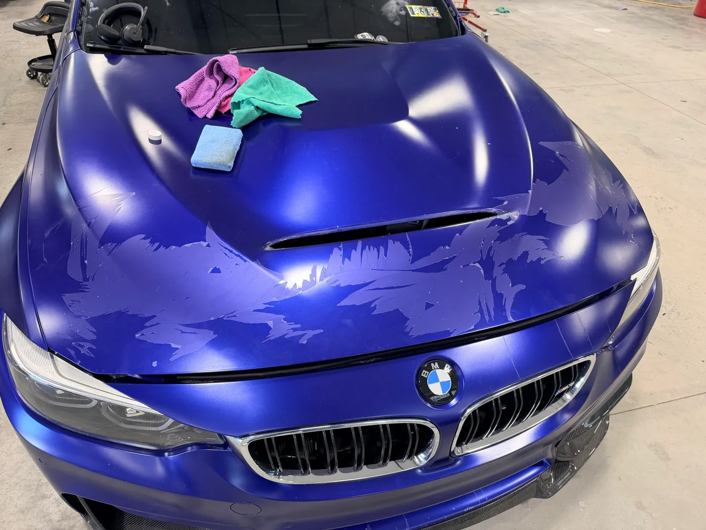 Sheet paint protection film part way through removal on a blue BMW M3 hood, tearing into strips