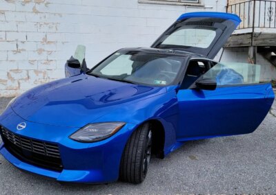 A car with shiny blue paint being detailed by a worker in a red shirt.