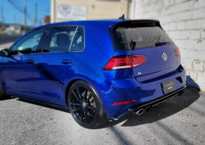 A car with open hood being detailed by a worker in a garage.
