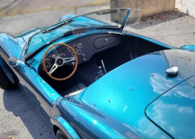 Car with open hood being detailed by a person in a red shirt at Total Detailing.