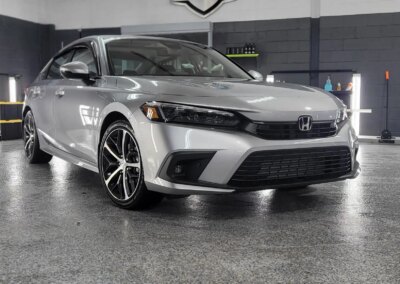 A shiny black car being detailed by a person in a red shirt.