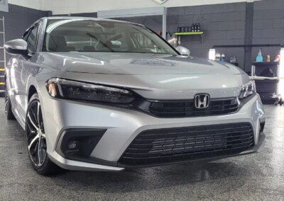 Black shiny car being detailed by a worker with a cloth in a workshop.