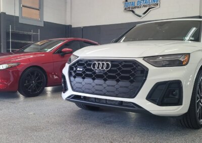 A car with open doors and hood being detailed by a worker in a garage.