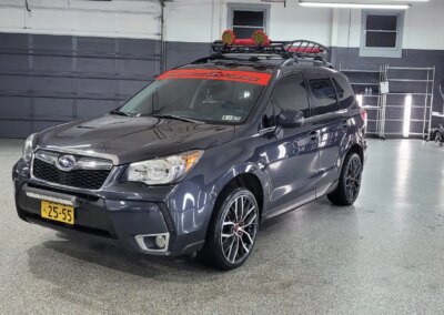 A car with shiny black paint getting detailed by a worker with a polishing machine.