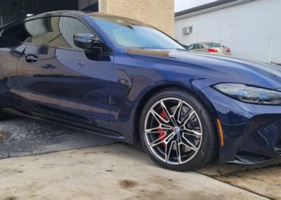 A person detailing a black car with cleaning products and microfiber towels.
