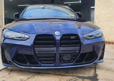 A car with shiny black paint being detailed by a worker in a red shirt.