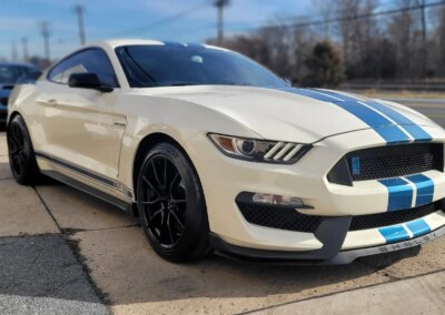 A silver car with open hood receiving detailing service in a garage.