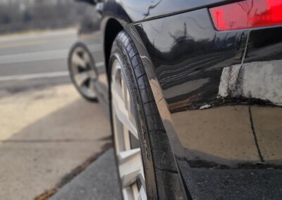 A shiny black car after detailing service with clean wheels and glossy paint.